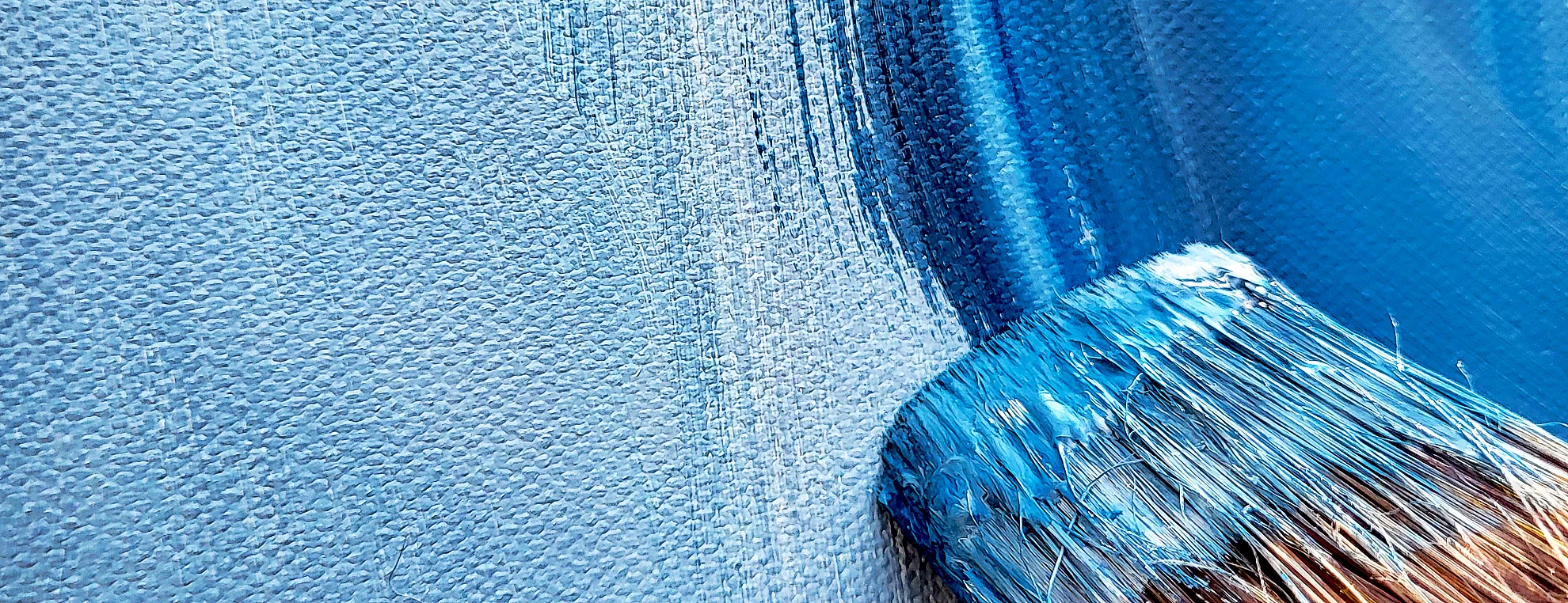 Close-up of paintbrush applying blue paint to canvas
