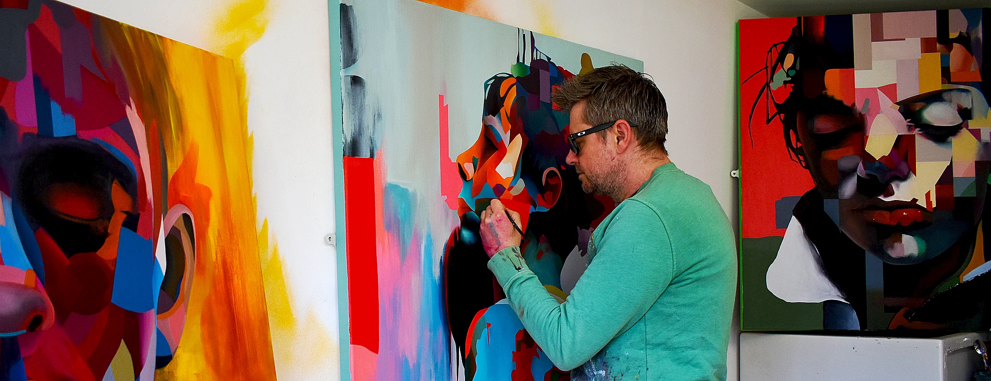 Abstract portrait artist Paul Kneen painting in studio surrounded by colourful canvases
