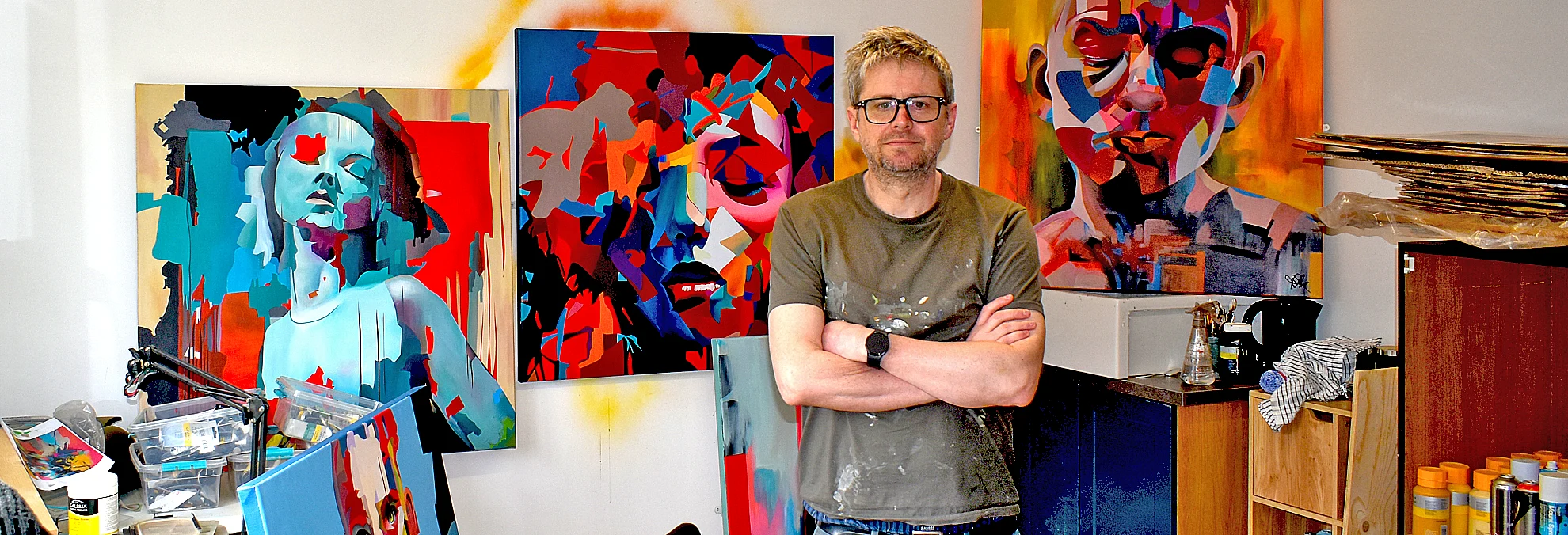 Paul Kneen standing in his studio surrounded by abstract portrait paintings